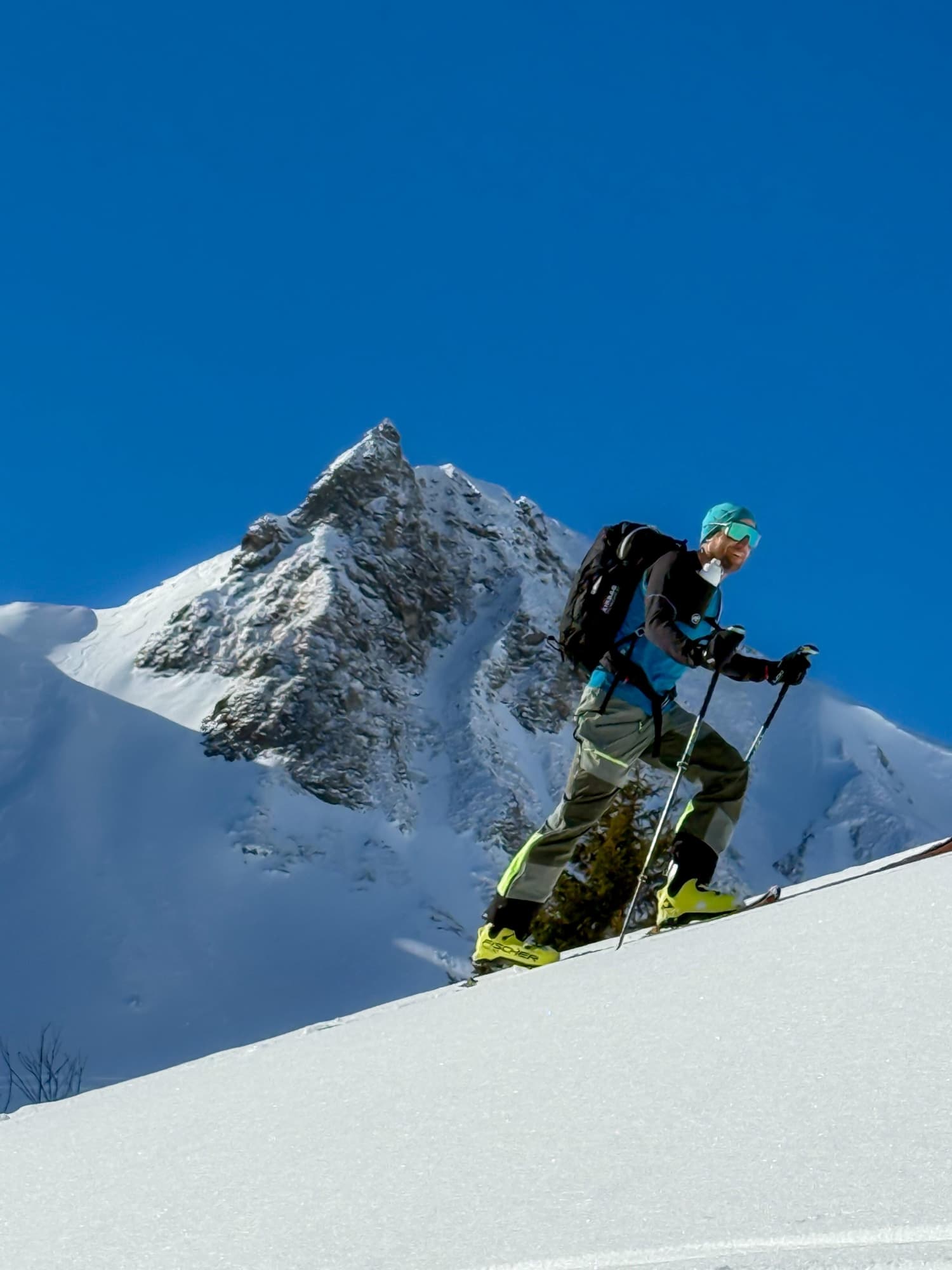 A portrait of Marina. She is wearing the Antelope EMS suit and smiling at the camera. Behind her are snow-covered mountains.