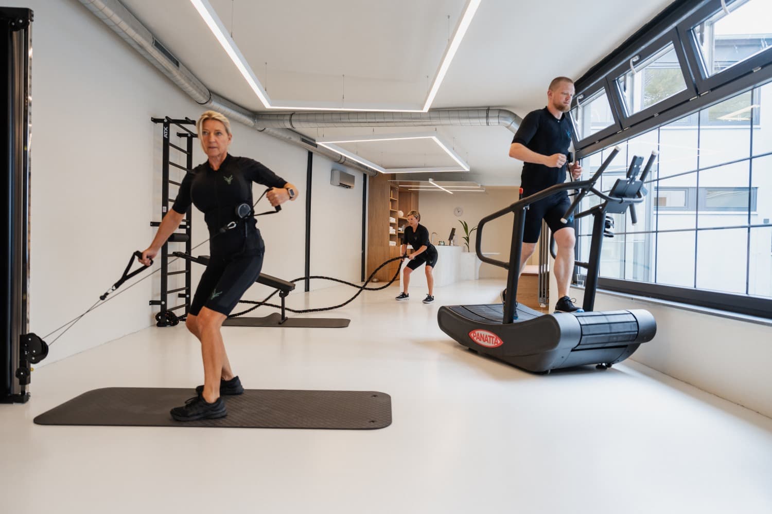 A picture of 3 people in the Antelope EMS suit in a fitness studio. They are all doing different exercises.